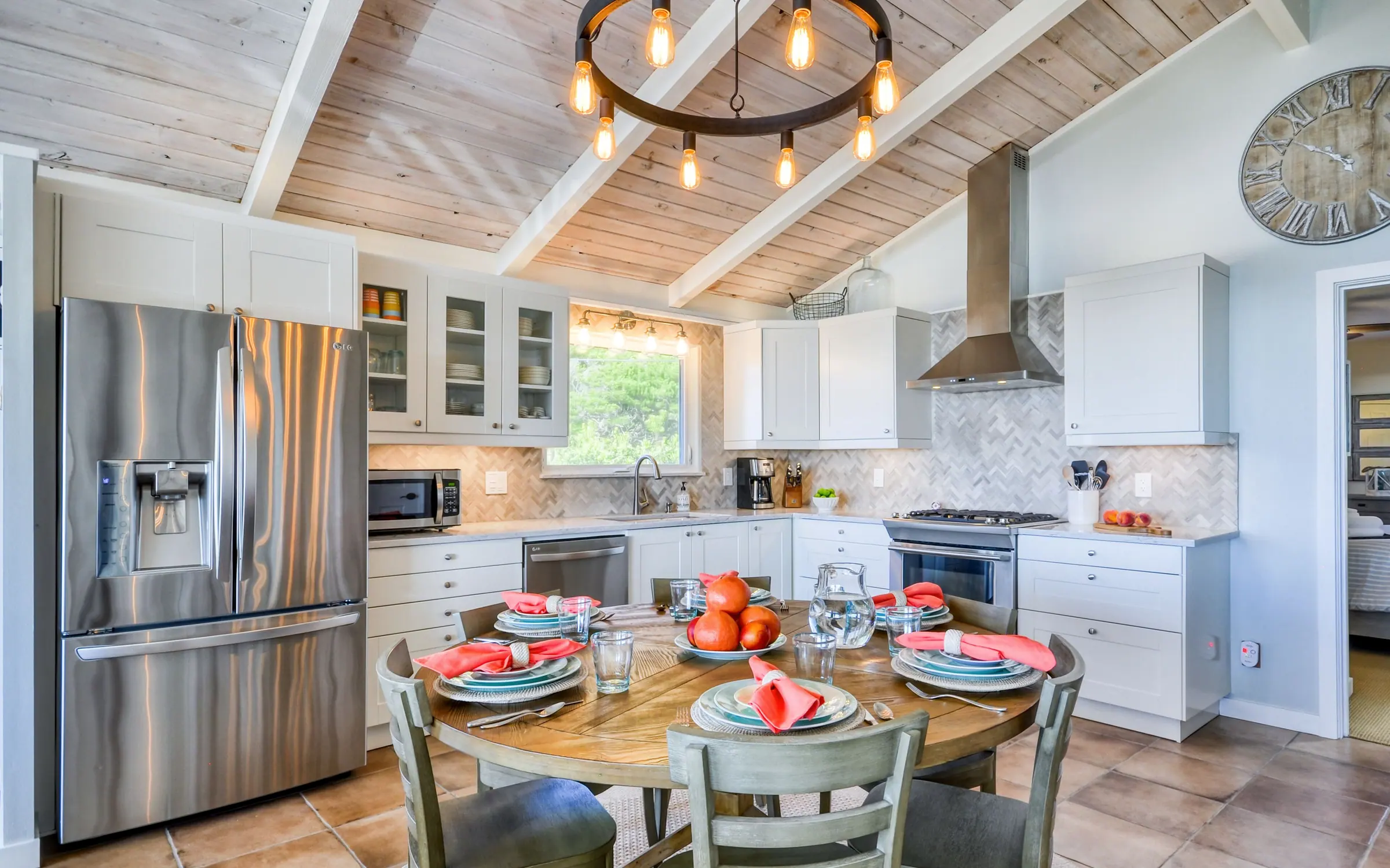 The kitchen: white shaker cabinets with glass uppers, a herringbone tile backsplash, stainless gas range and hood, dishwasher and french-door refrigerator, under the same whitewashed plank ceiling and iron ring chandelier.