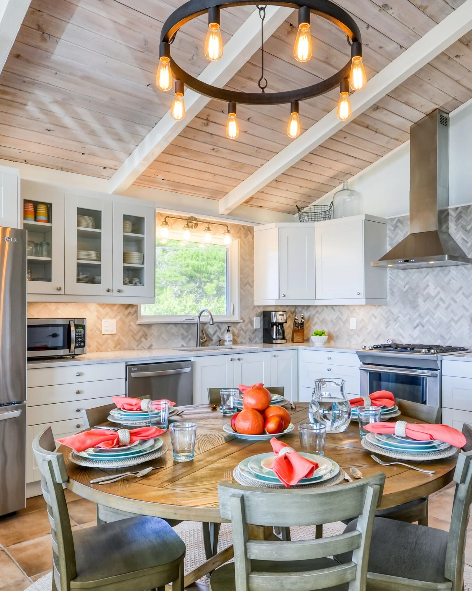 The kitchen: white shaker cabinets with glass uppers, a herringbone tile backsplash, stainless gas range and hood, dishwasher and french-door refrigerator, under the same whitewashed plank ceiling and iron ring chandelier.
